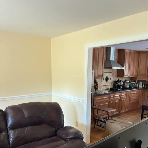 Finished neutral interior room with white chair rail and adjoining kitchen